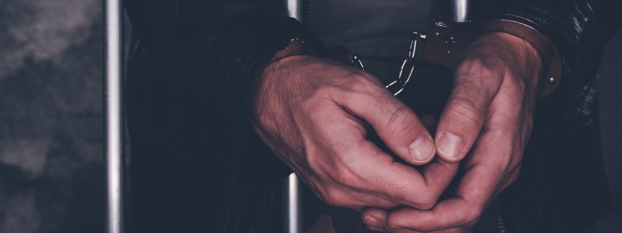Handcuffed man behind prison bars. Arrested criminal male person imprisoned.