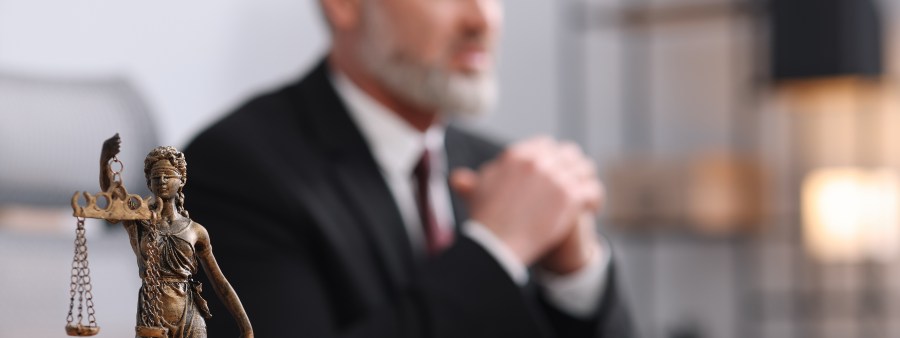 Notary in suit at wooden table in office, focus on statue of Lady Justice